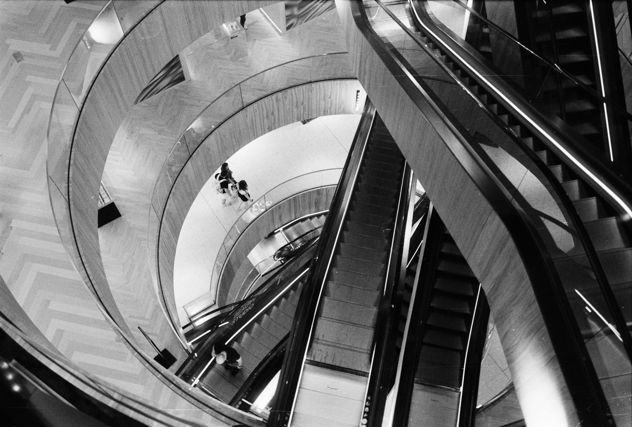 Escalators crossing a circular multi-storey atrium, shoppers on the levels below.